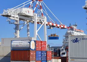 Colorful shipping containers stacked in a busy port with cranes overhead.